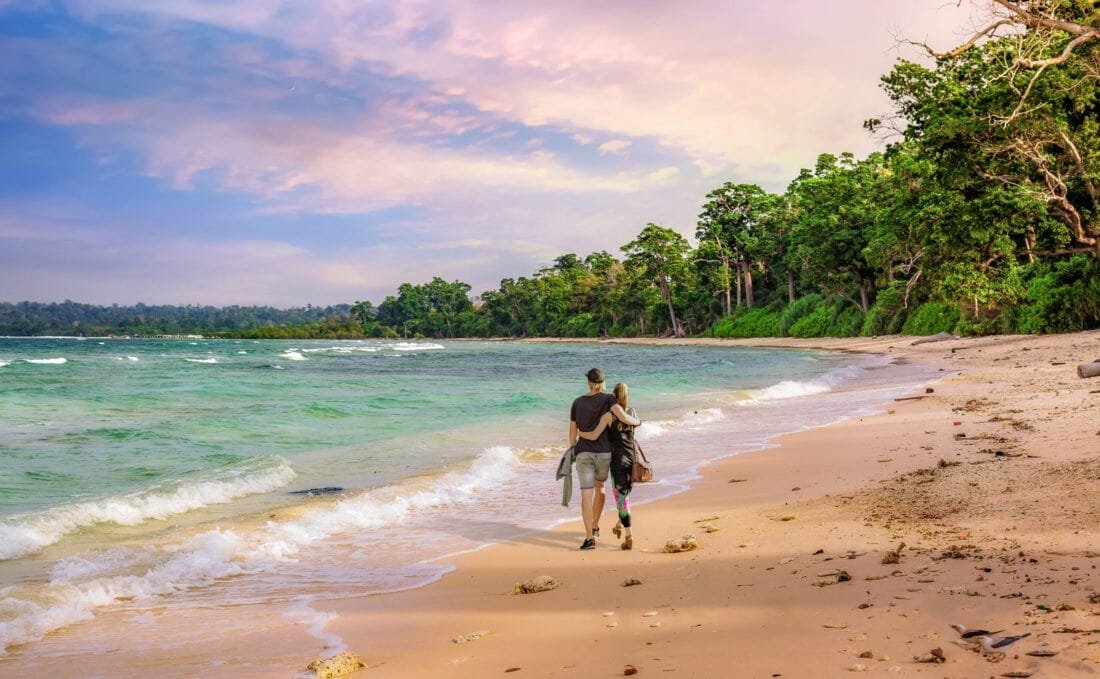 Scenic view of pristine white-sand beaches at Havelock Island, Andaman & Nicobar, with clear turquoise water, palm trees, and bright skies. Part of the Andaman & Nicobar 8N9D Budget Tour Package